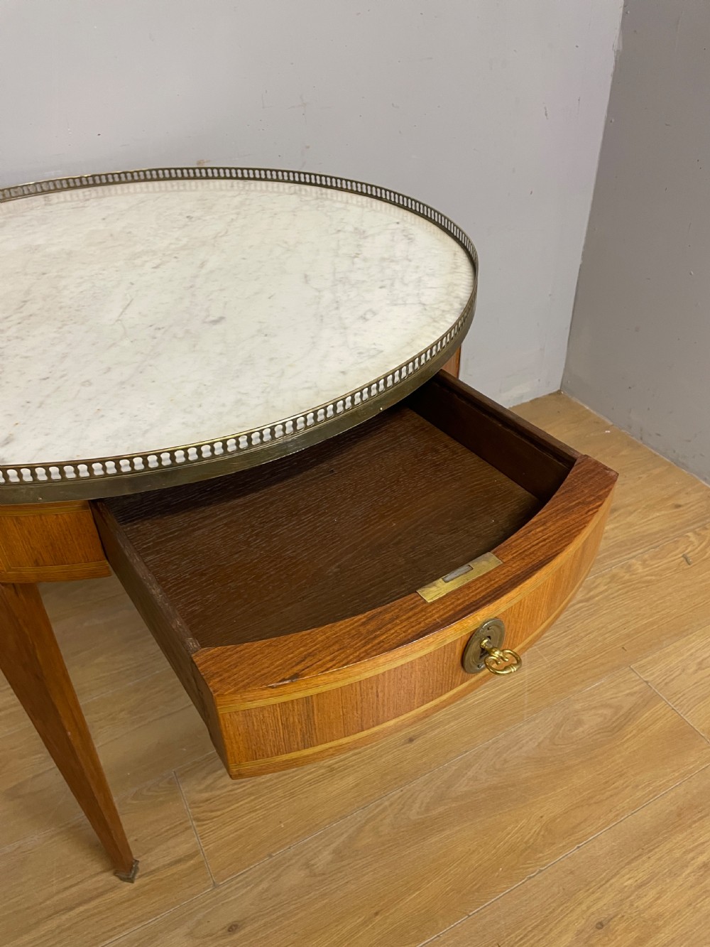 A late 19th-century French circular Bouillotte table featuring a white marble top with a pierced brass gallery, a veneered apron with a small drawer, and four square tapered legs ending in brass sabots. View V