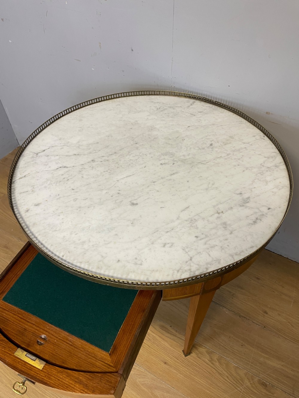 A late 19th-century French circular Bouillotte table featuring a white marble top with a pierced brass gallery, a veneered apron with a small drawer, and four square tapered legs ending in brass sabots. View VI