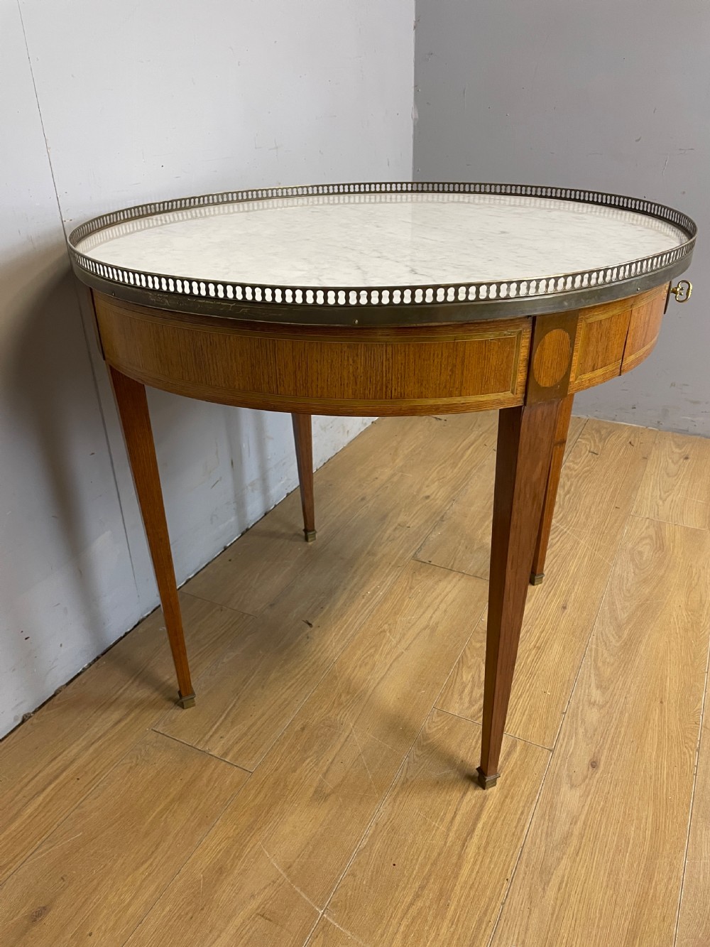 A late 19th-century French circular Bouillotte table featuring a white marble top with a pierced brass gallery, a veneered apron with a small drawer, and four square tapered legs ending in brass sabots. View VIII