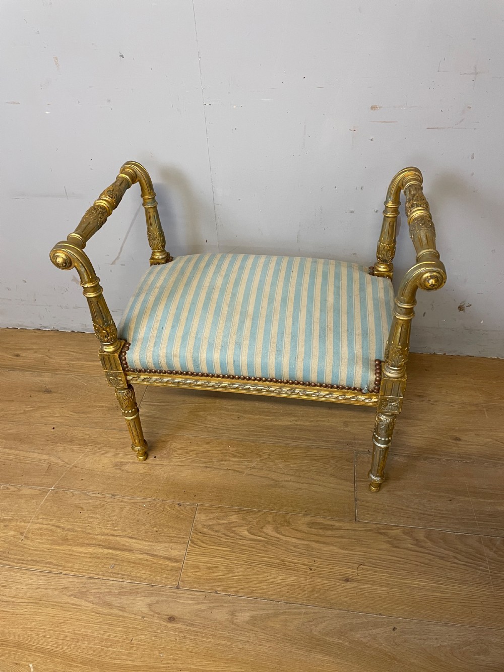 A Louis XVI style French giltwood window seat featuring rolled arms, fluted tapering legs, and blue and cream striped upholstery. View II