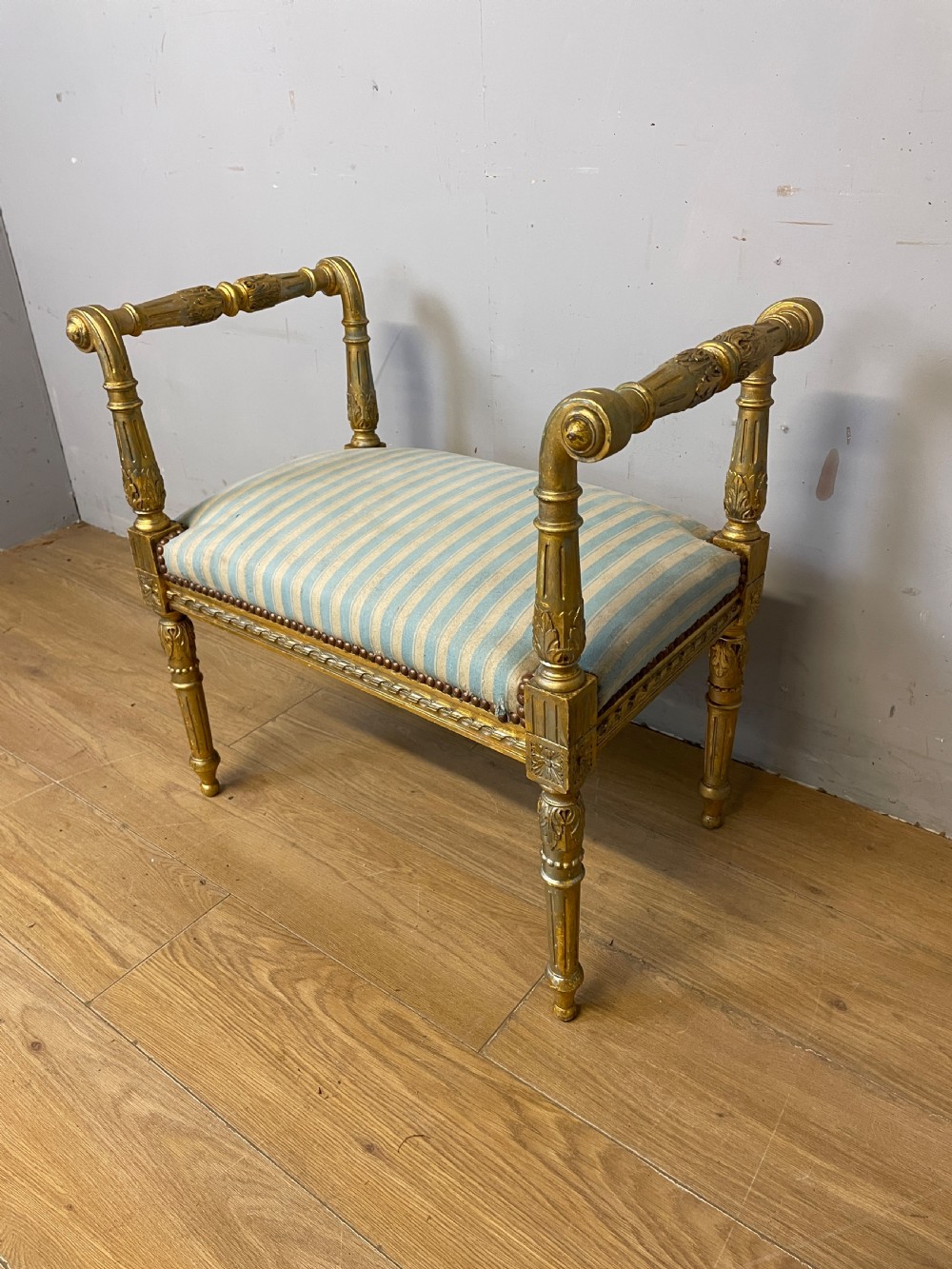 A Louis XVI style French giltwood window seat featuring rolled arms, fluted tapering legs, and blue and cream striped upholstery. View IV
