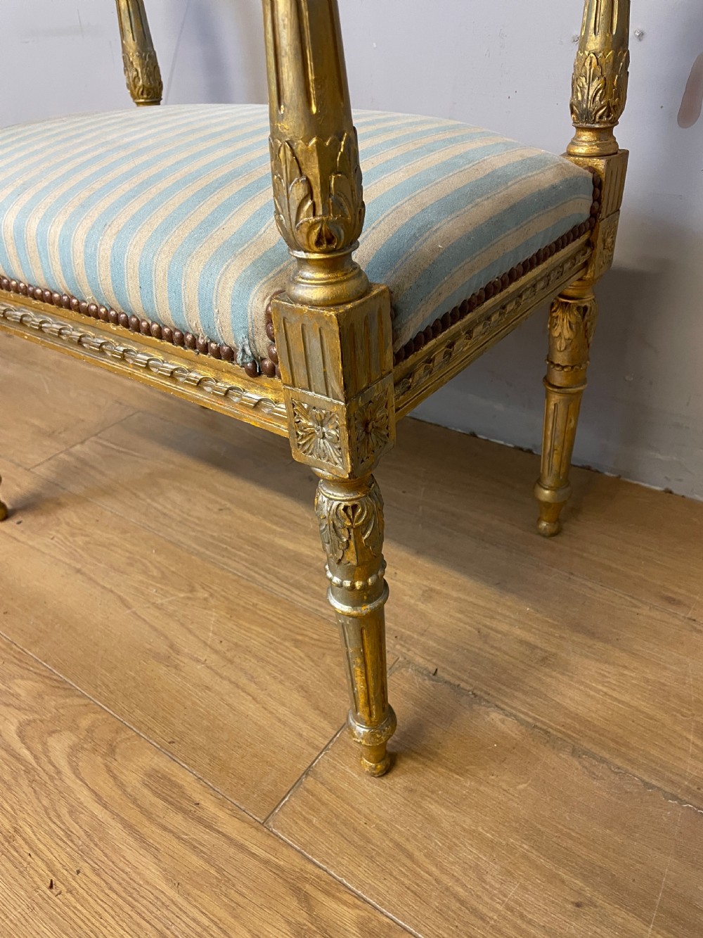 A Louis XVI style French giltwood window seat featuring rolled arms, fluted tapering legs, and blue and cream striped upholstery. View V