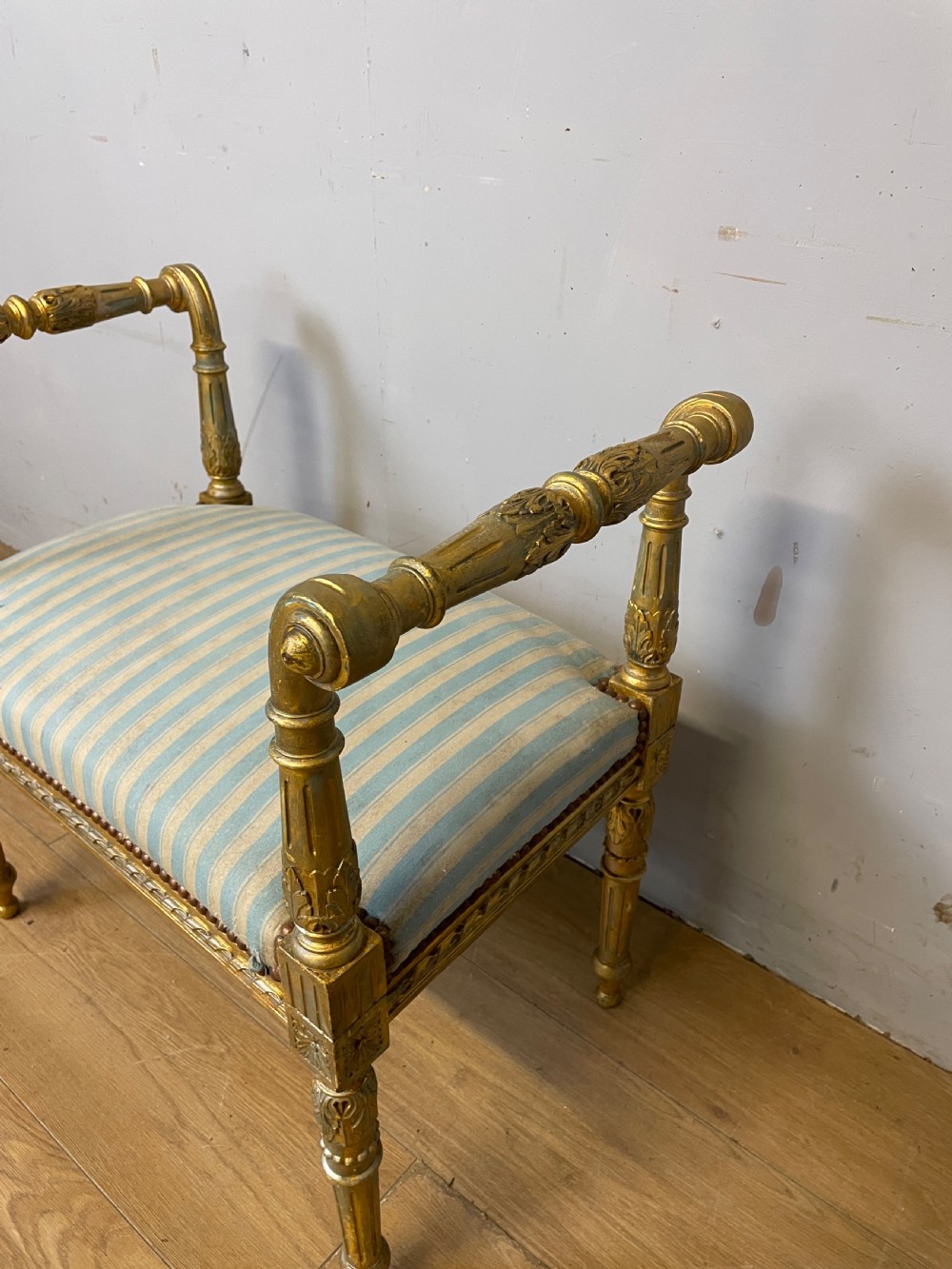 A Louis XVI style French giltwood window seat featuring rolled arms, fluted tapering legs, and blue and cream striped upholstery. View VI