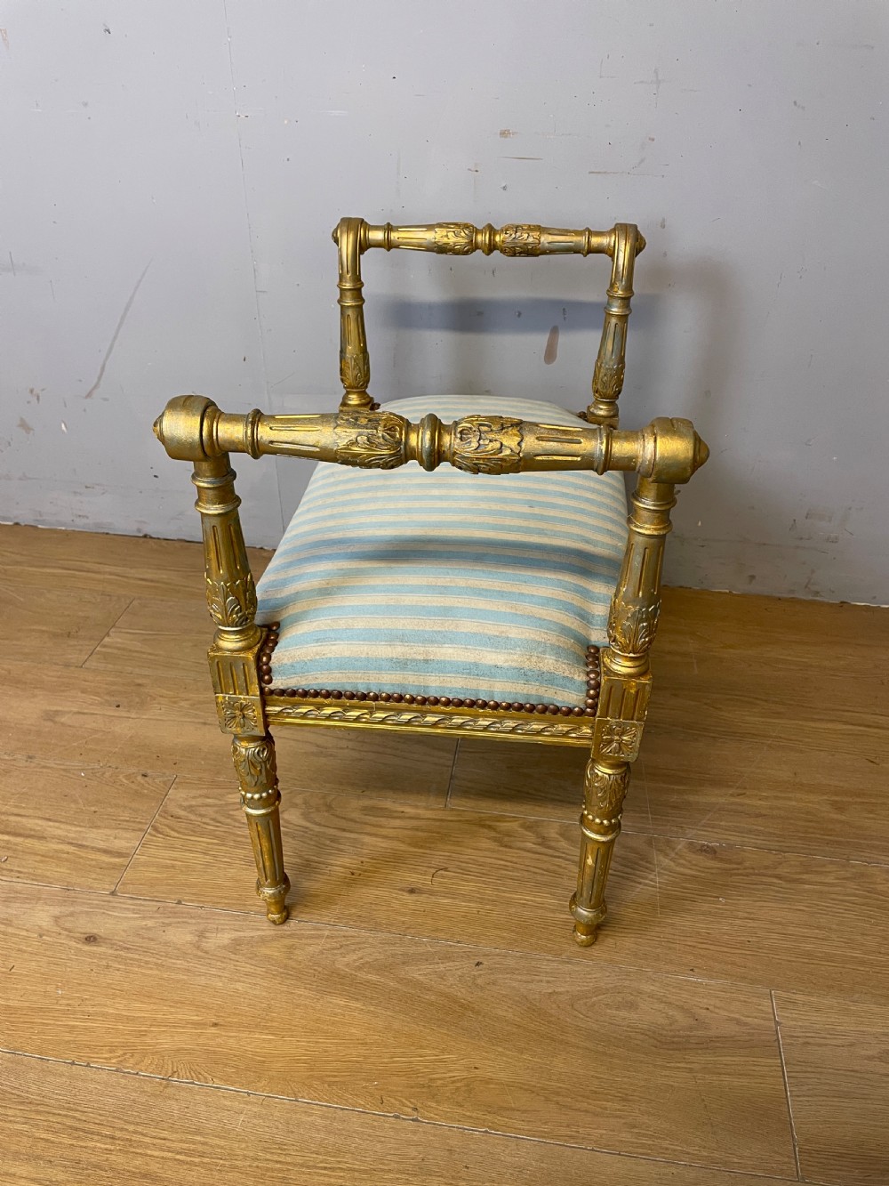 A Louis XVI style French giltwood window seat featuring rolled arms, fluted tapering legs, and blue and cream striped upholstery. View VIII