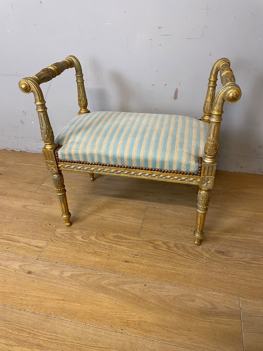 A Louis XVI style French giltwood window seat featuring rolled arms, fluted tapering legs, and blue and cream striped upholstery. View IX