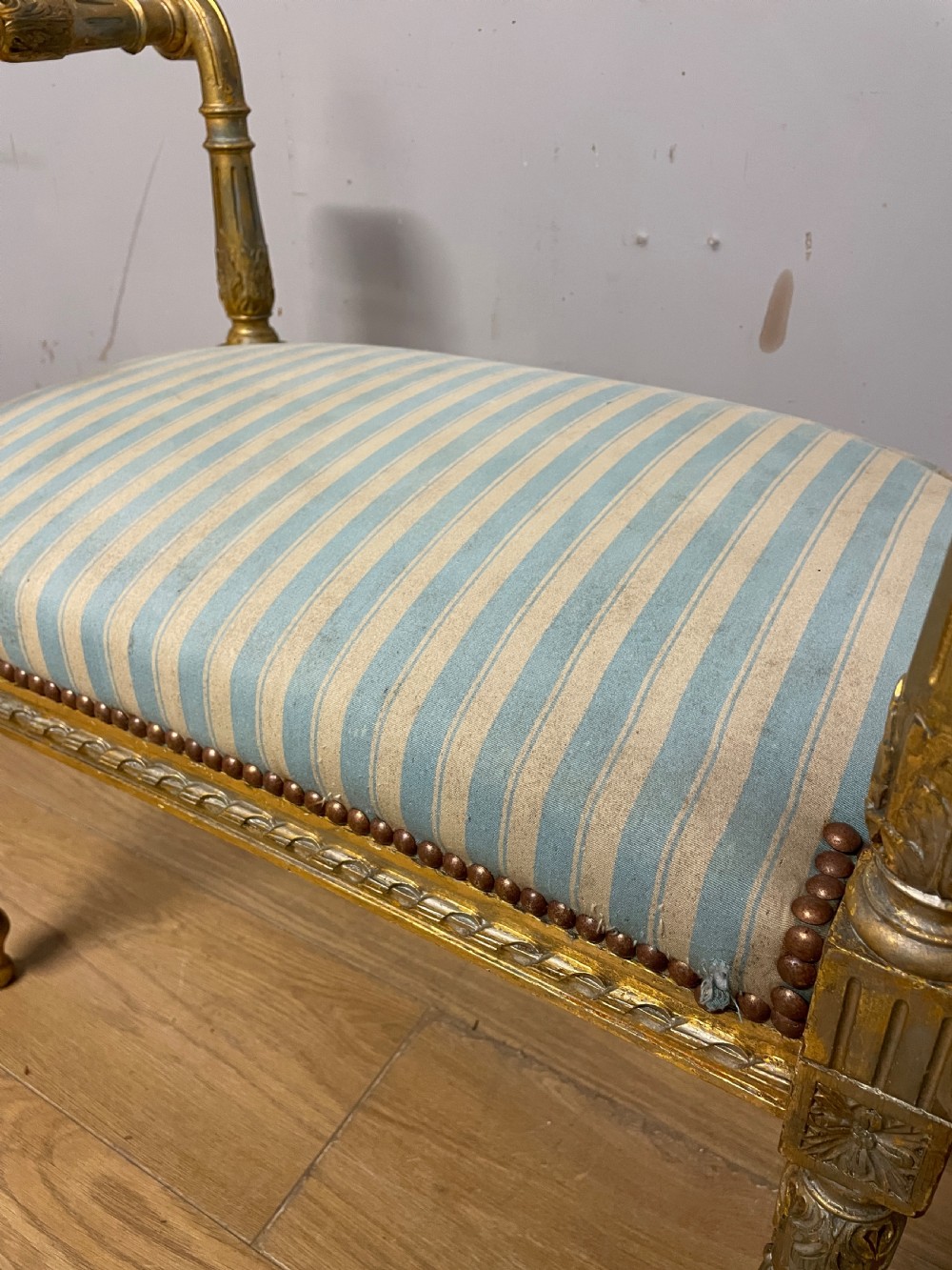 A Louis XVI style French giltwood window seat featuring rolled arms, fluted tapering legs, and blue and cream striped upholstery. View XIV