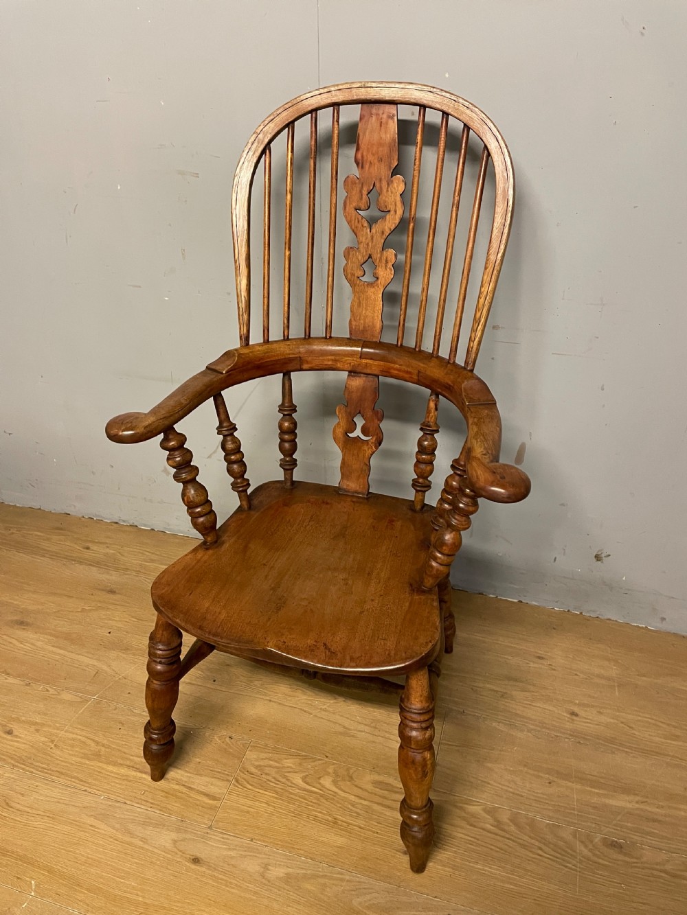 A 19th-century ash and elm Windsor armchair featuring a hoop back, pierced central splat, turned arm supports, and a solid contoured seat.