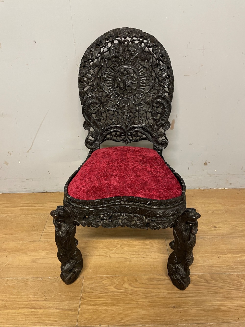 A 19th-century Burmese side chair featuring an intricately carved dark wood openwork backrest and animal-shaped cabriole legs with a red velvet upholstered seat.