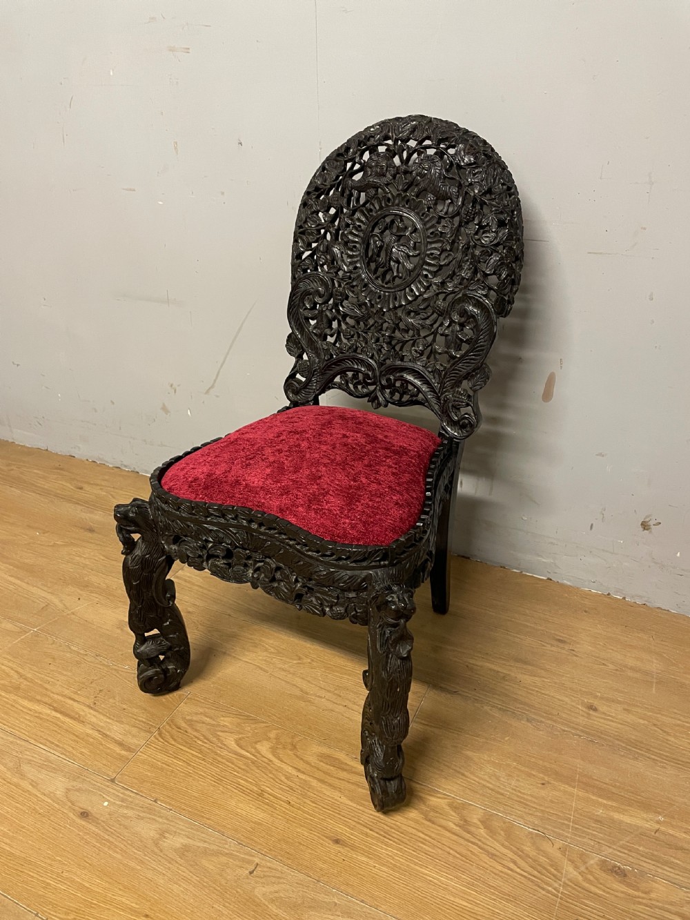 A 19th-century Burmese side chair featuring an intricately carved dark wood openwork backrest and animal-shaped cabriole legs with a red velvet upholstered seat. View II