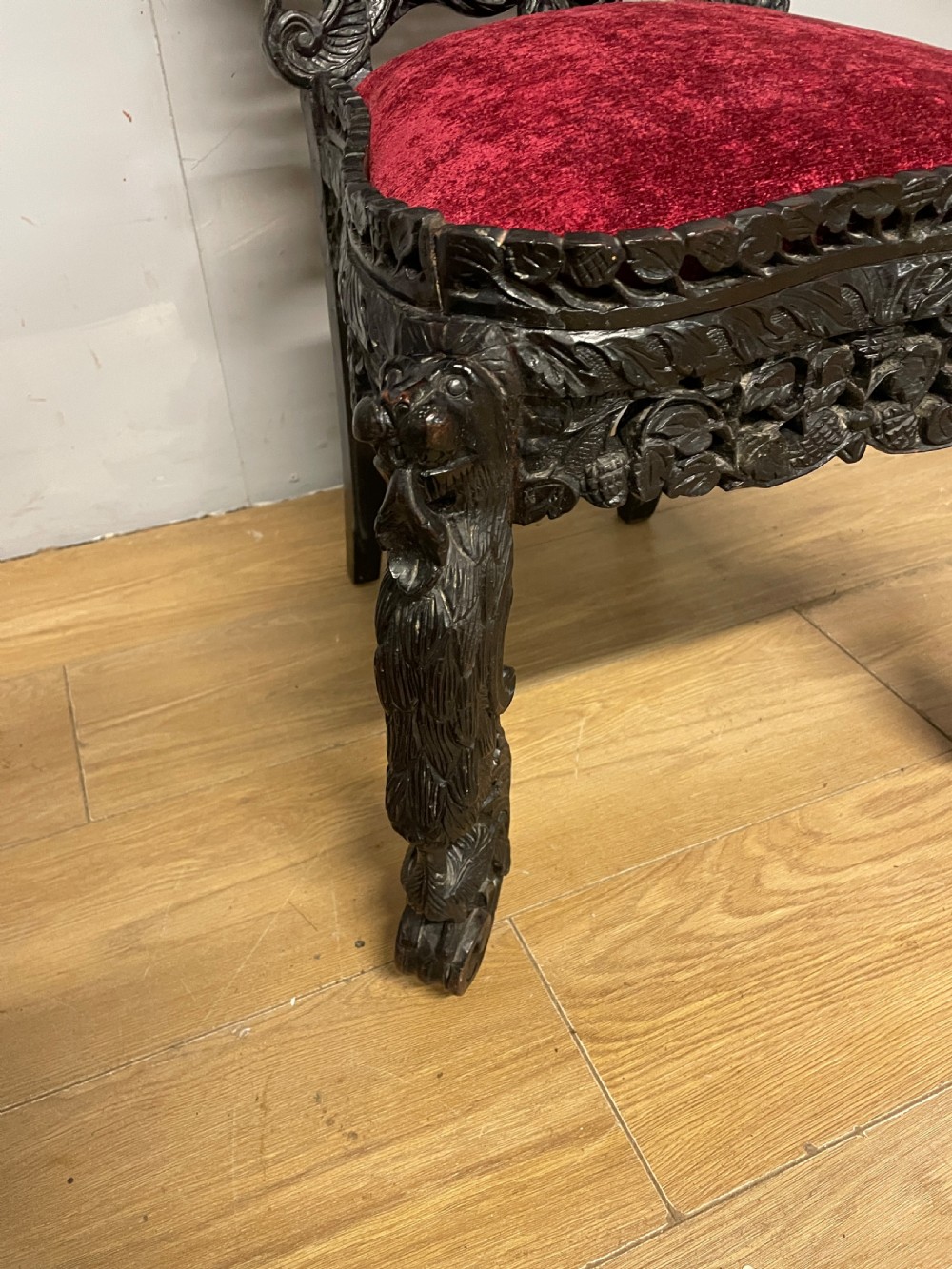 A 19th-century Burmese side chair featuring an intricately carved dark wood openwork backrest and animal-shaped cabriole legs with a red velvet upholstered seat. View V