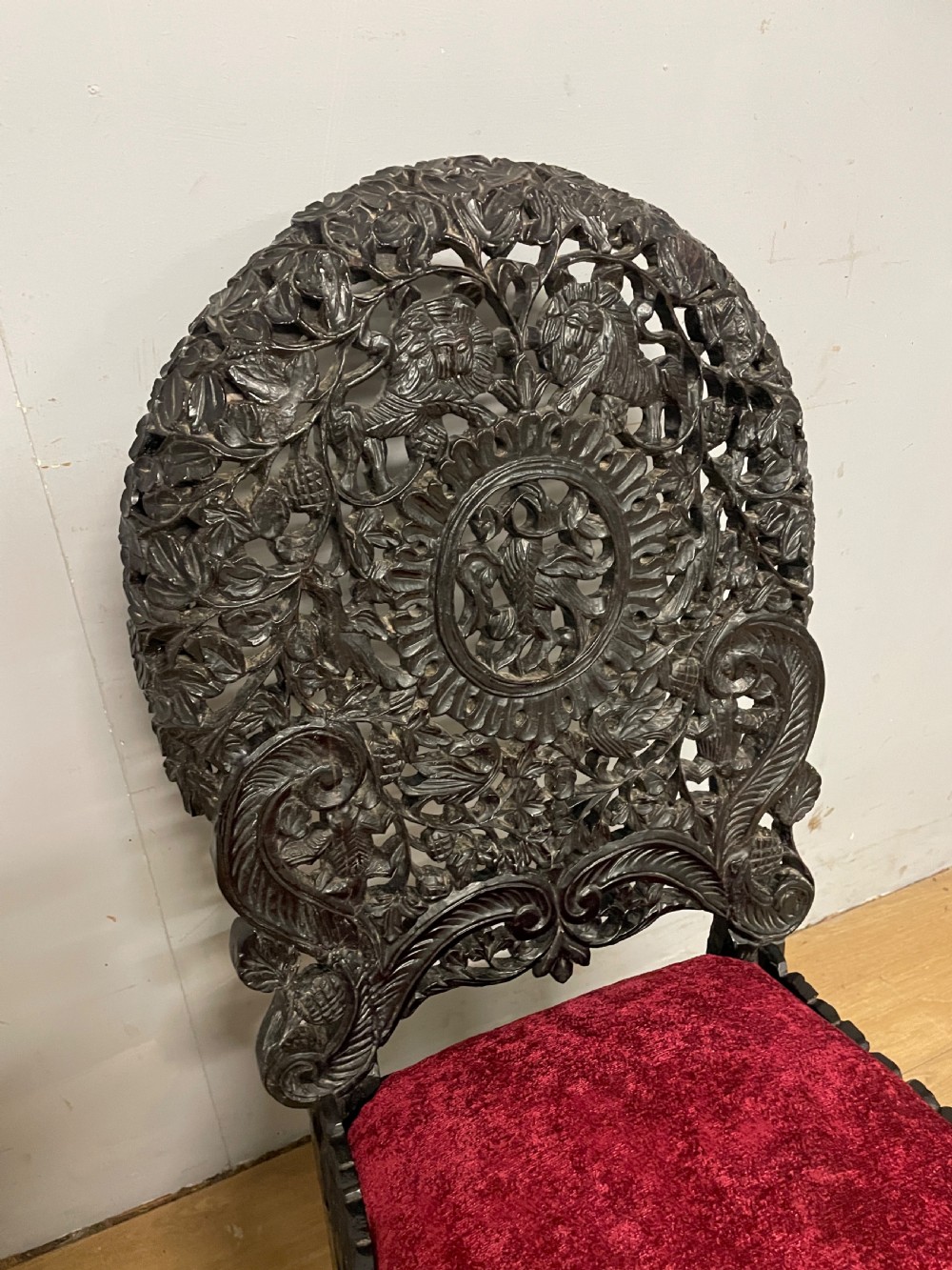 A 19th-century Burmese side chair featuring an intricately carved dark wood openwork backrest and animal-shaped cabriole legs with a red velvet upholstered seat. View VI