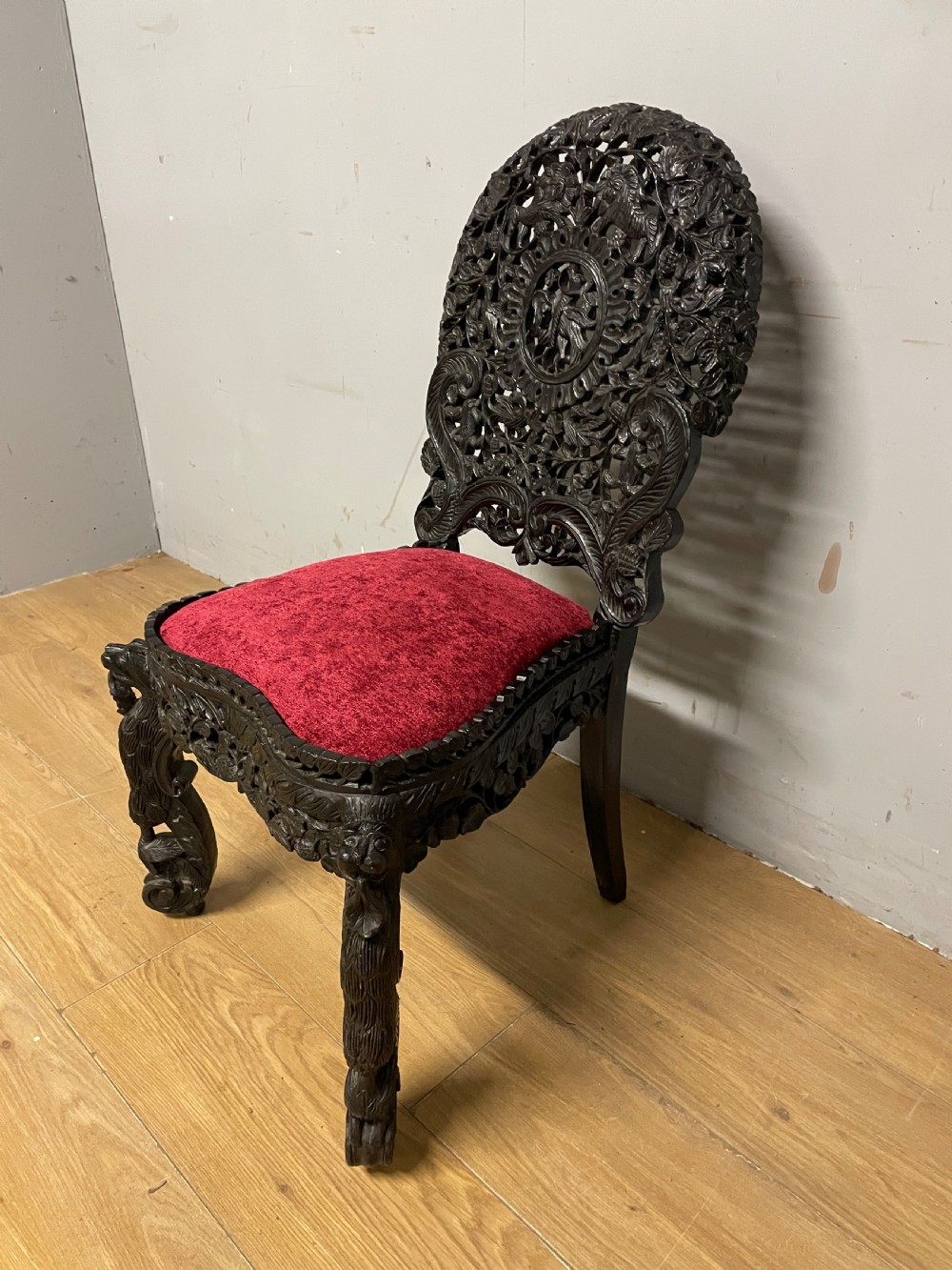 A 19th-century Burmese side chair featuring an intricately carved dark wood openwork backrest and animal-shaped cabriole legs with a red velvet upholstered seat. View VIII