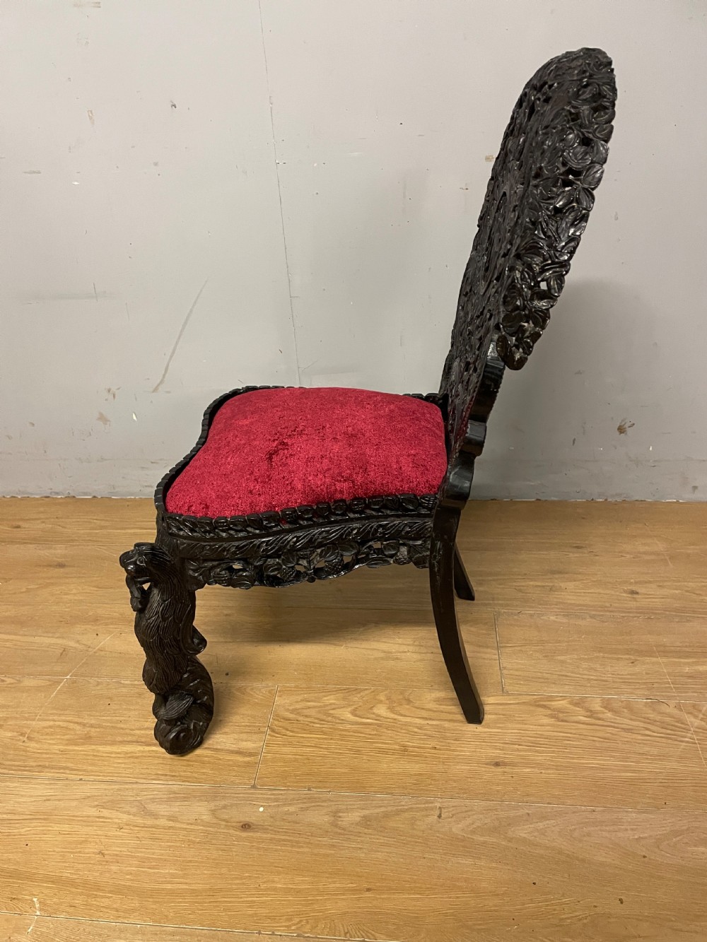 A 19th-century Burmese side chair featuring an intricately carved dark wood openwork backrest and animal-shaped cabriole legs with a red velvet upholstered seat. View IX