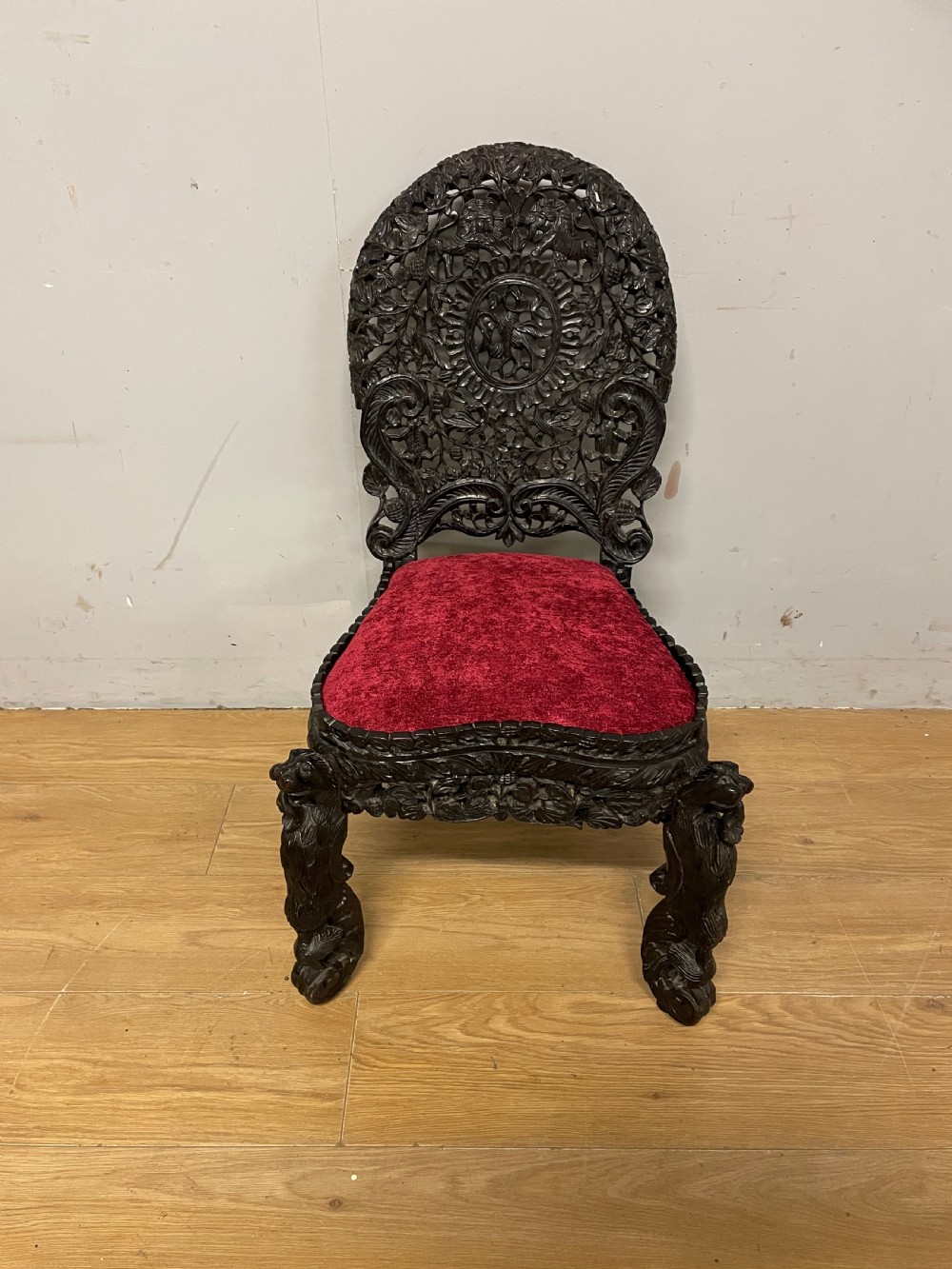 A 19th-century Burmese side chair featuring an intricately carved dark wood openwork backrest and animal-shaped cabriole legs with a red velvet upholstered seat. View XII