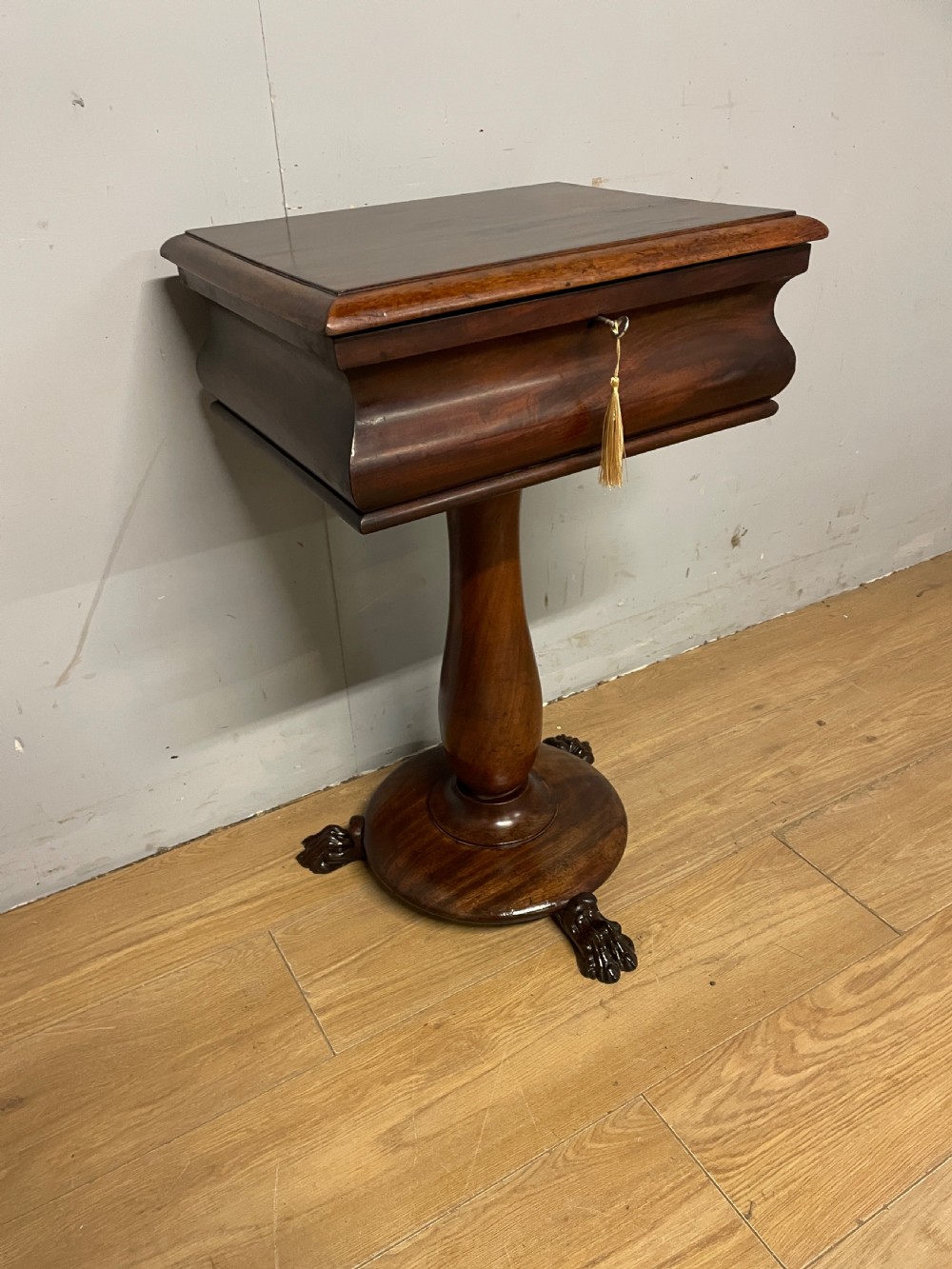 A Regency flame mahogany work table featuring a curved apron, central turned pedestal, circular plinth, and carved lion paw feet.