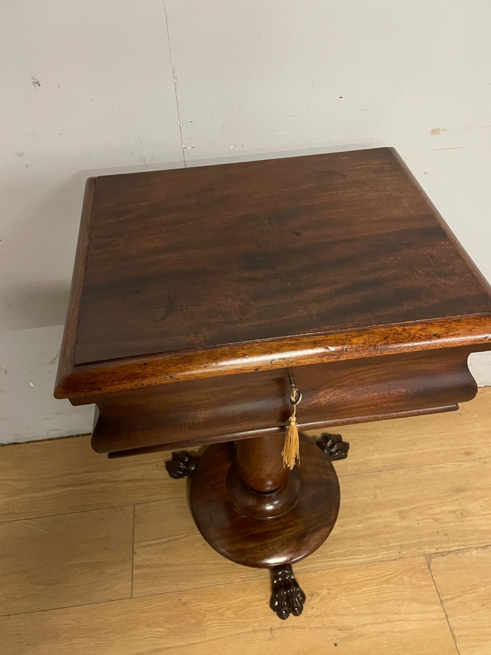 A Regency flame mahogany work table featuring a curved apron, central turned pedestal, circular plinth, and carved lion paw feet. View V