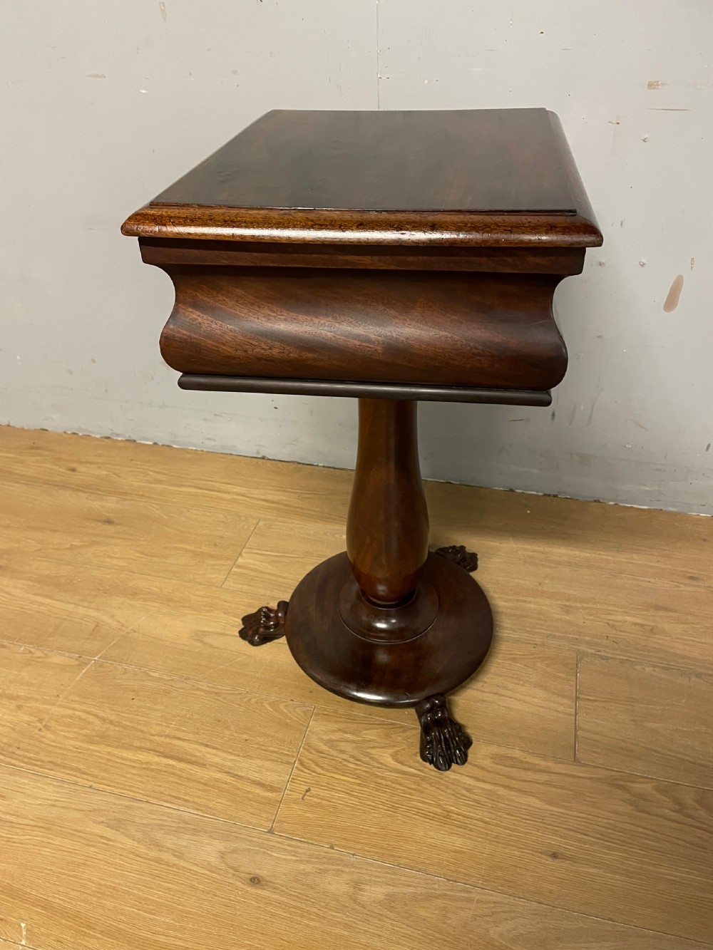 A Regency flame mahogany work table featuring a curved apron, central turned pedestal, circular plinth, and carved lion paw feet. View X
