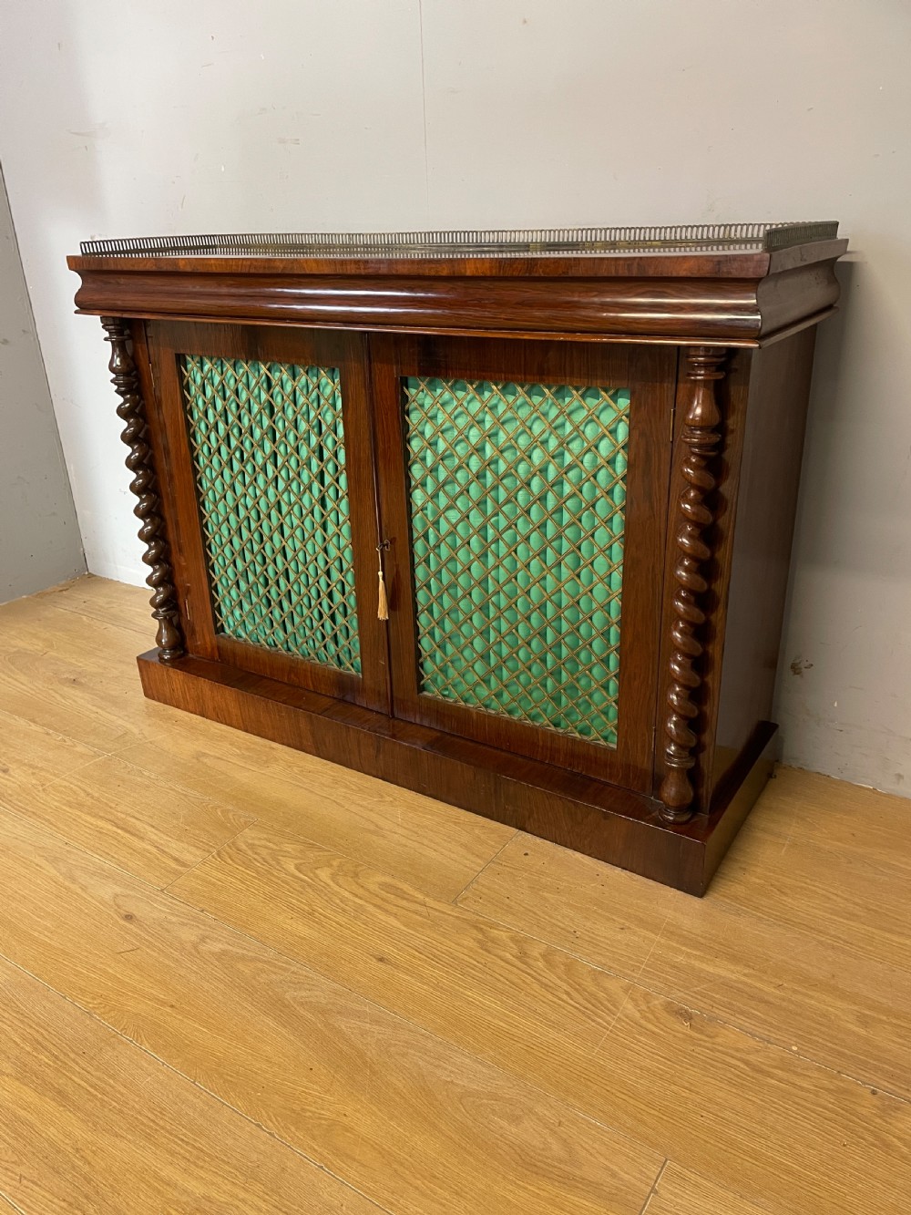 A late Regency rosewood chiffonier featuring barley twist columns, brass wire lattice doors backed with green pleated fabric, and a brass gallery top rail. View III