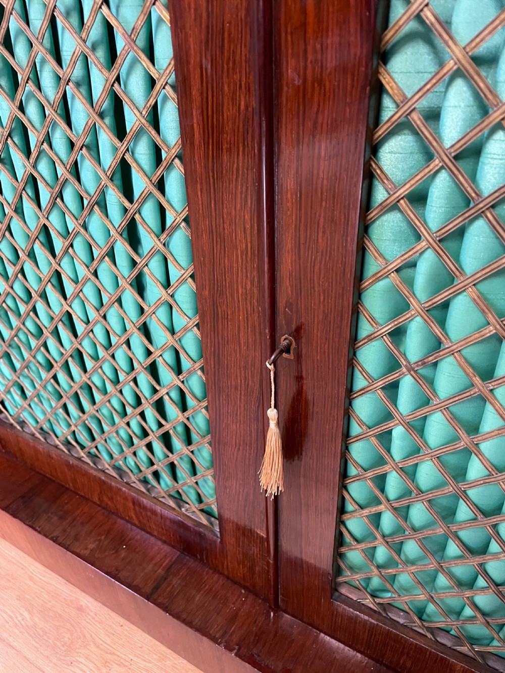 A late Regency rosewood chiffonier featuring barley twist columns, brass wire lattice doors backed with green pleated fabric, and a brass gallery top rail. View V