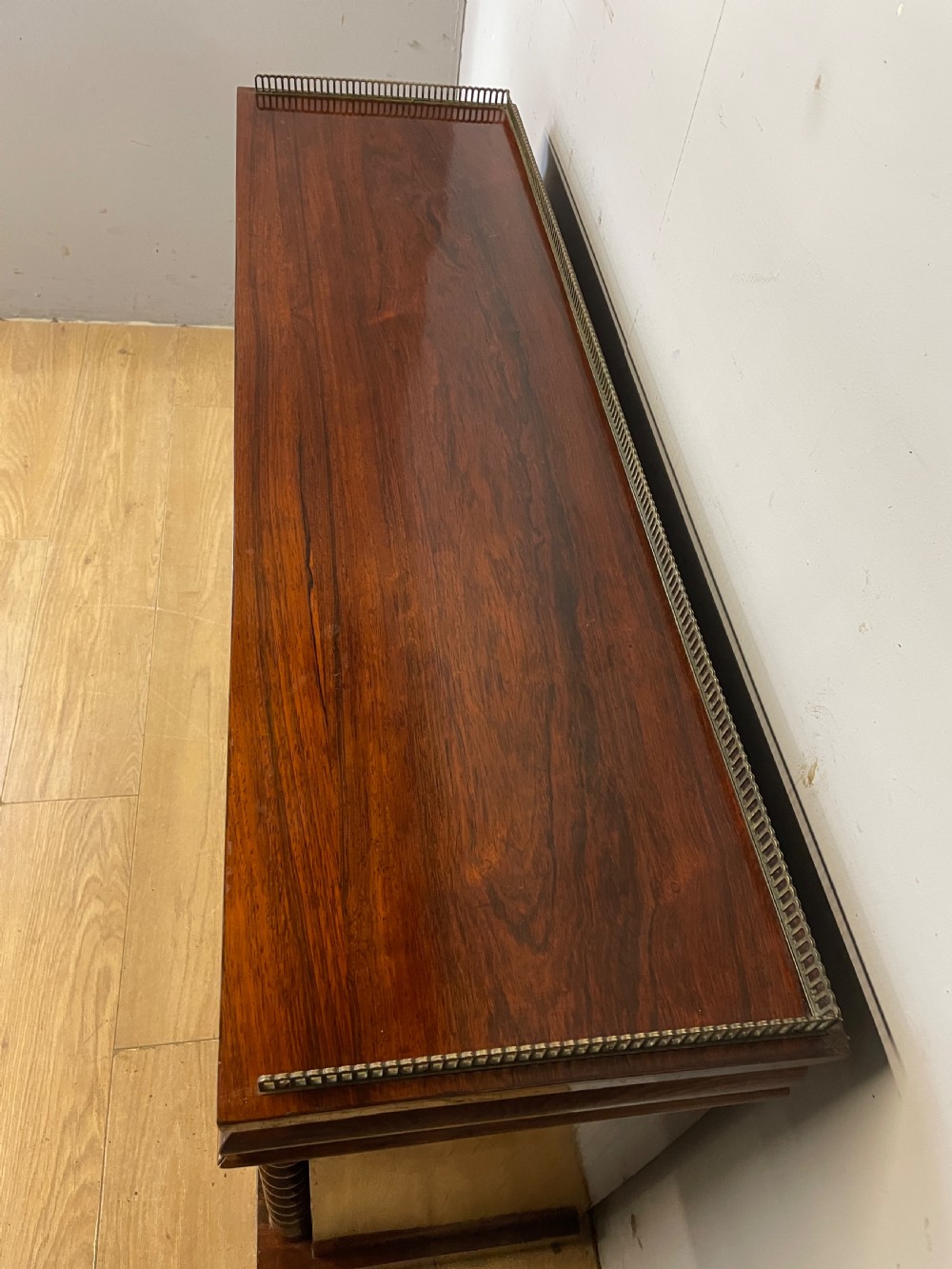 A late Regency rosewood chiffonier featuring barley twist columns, brass wire lattice doors backed with green pleated fabric, and a brass gallery top rail. View VIII