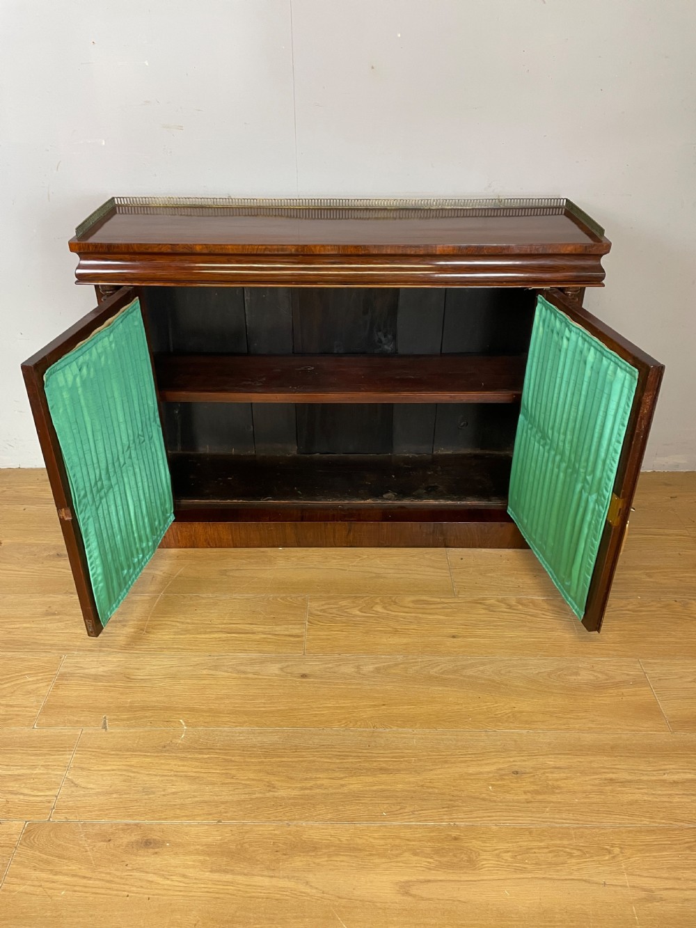 A late Regency rosewood chiffonier featuring barley twist columns, brass wire lattice doors backed with green pleated fabric, and a brass gallery top rail. View IX
