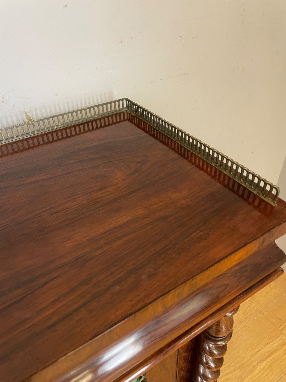A late Regency rosewood chiffonier featuring barley twist columns, brass wire lattice doors backed with green pleated fabric, and a brass gallery top rail. View XII