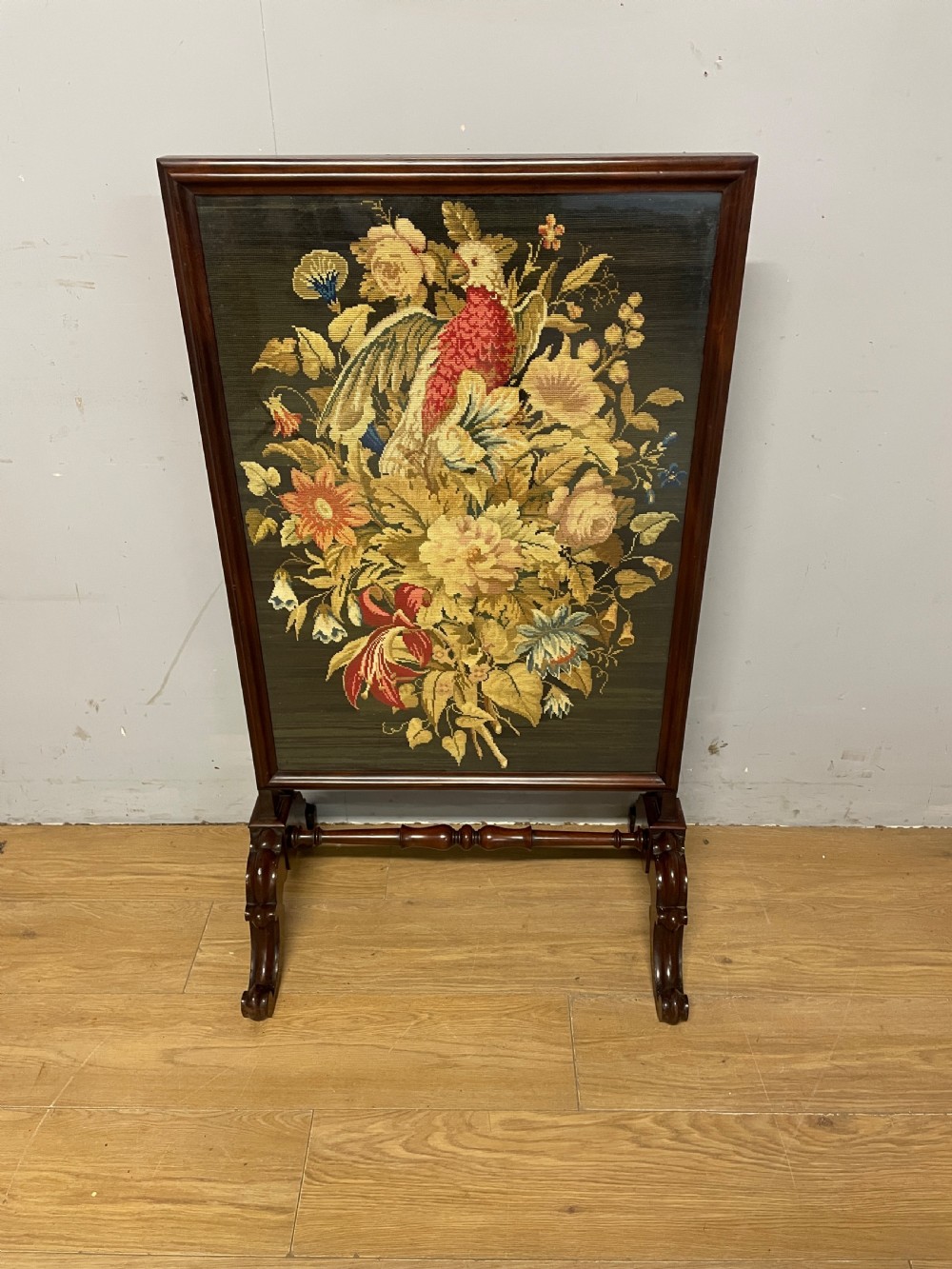 A nineteenth-century mahogany firescreen featuring a central needlepoint panel depicting a floral arrangement and bird, supported by carved splayed legs and a turned stretcher. View II