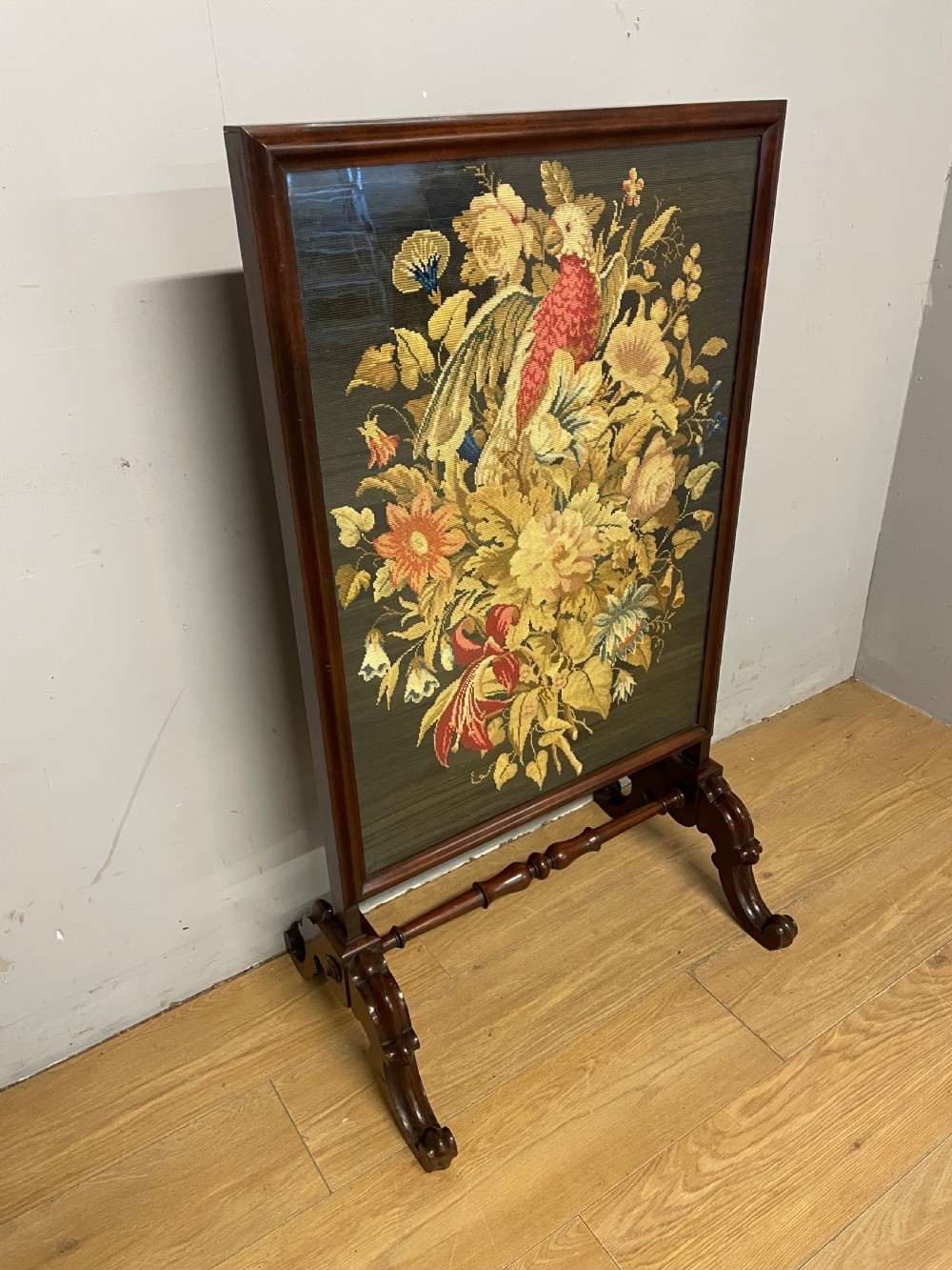 A nineteenth-century mahogany firescreen featuring a central needlepoint panel depicting a floral arrangement and bird, supported by carved splayed legs and a turned stretcher. View III
