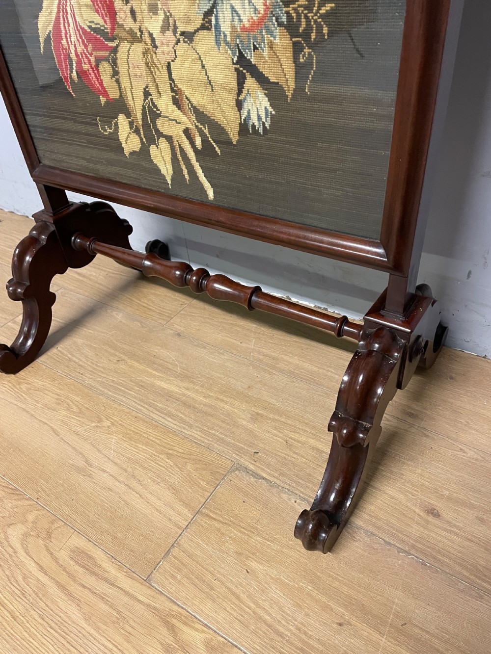 A nineteenth-century mahogany firescreen featuring a central needlepoint panel depicting a floral arrangement and bird, supported by carved splayed legs and a turned stretcher. View V