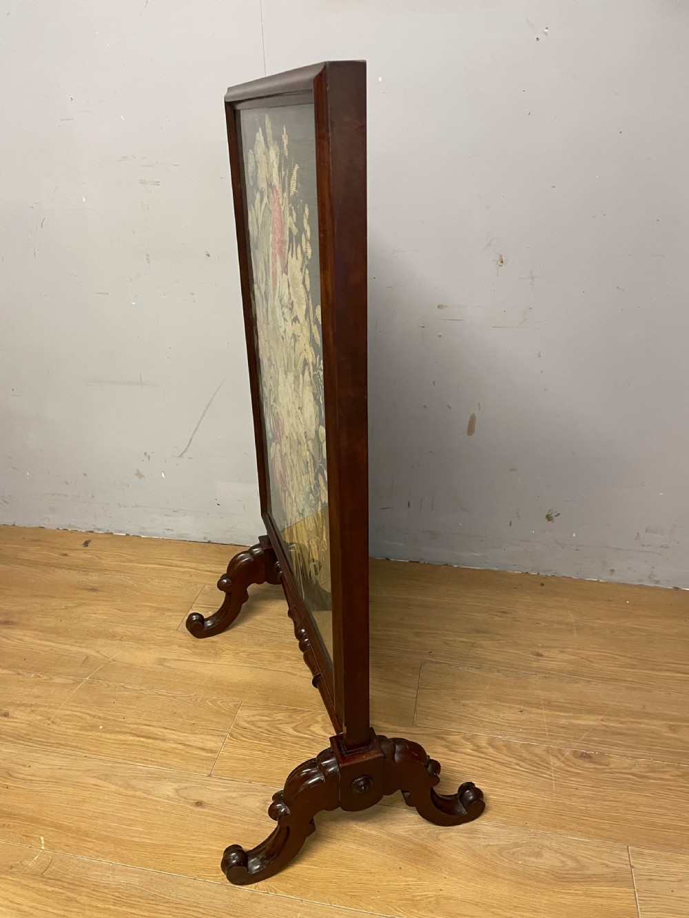 A nineteenth-century mahogany firescreen featuring a central needlepoint panel depicting a floral arrangement and bird, supported by carved splayed legs and a turned stretcher. View VIII