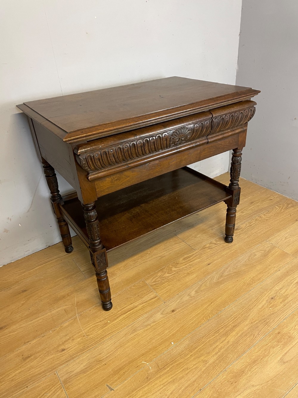 A 19th-century dark carved oak two-tier side table featuring turned legs and a detailed carved frieze.
