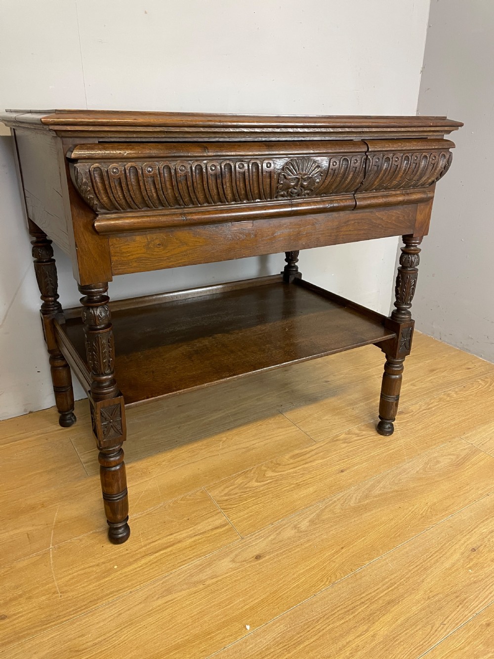 A 19th-century dark carved oak two-tier side table featuring turned legs and a detailed carved frieze. View II