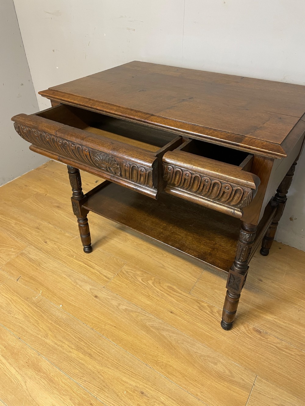 A 19th-century dark carved oak two-tier side table featuring turned legs and a detailed carved frieze. View V