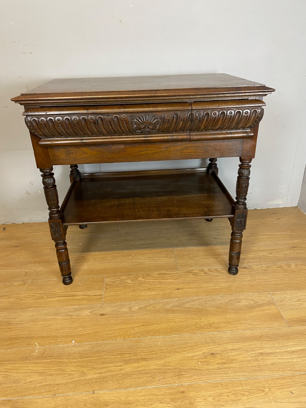 A 19th-century dark carved oak two-tier side table featuring turned legs and a detailed carved frieze. View X