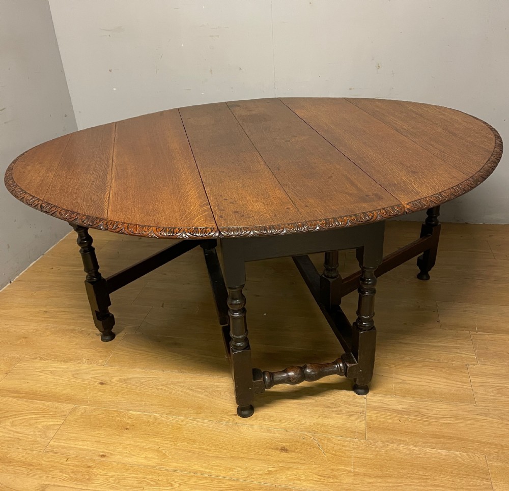 A large 19th-century dark oak drop-leaf dining table featuring turned gatelegs and a carved egg-and-dart motif along the oval table top border.