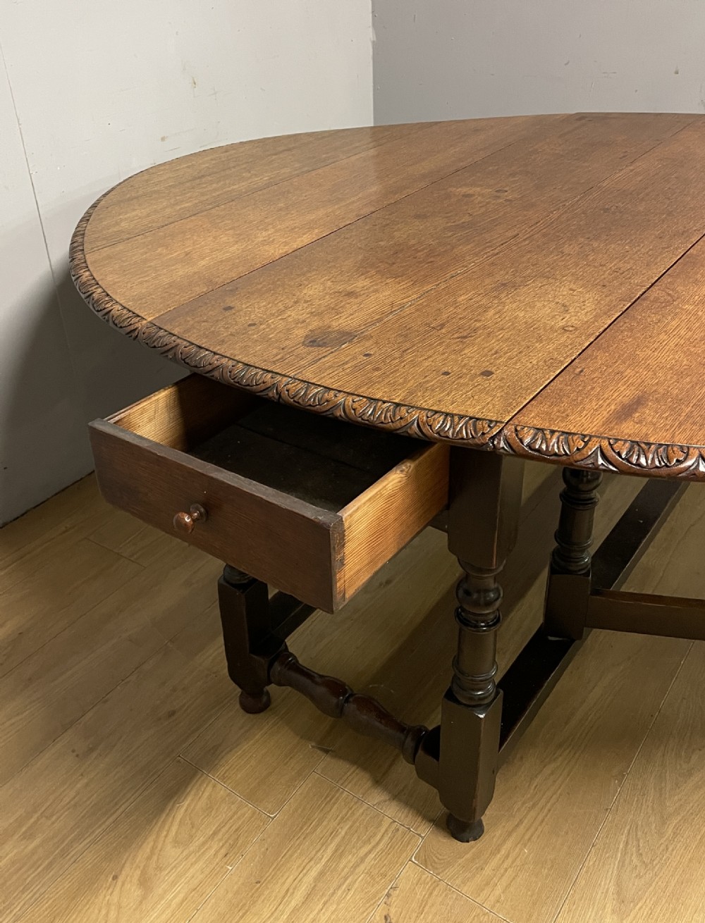 A large 19th-century dark oak drop-leaf dining table featuring turned gatelegs and a carved egg-and-dart motif along the oval table top border. View V