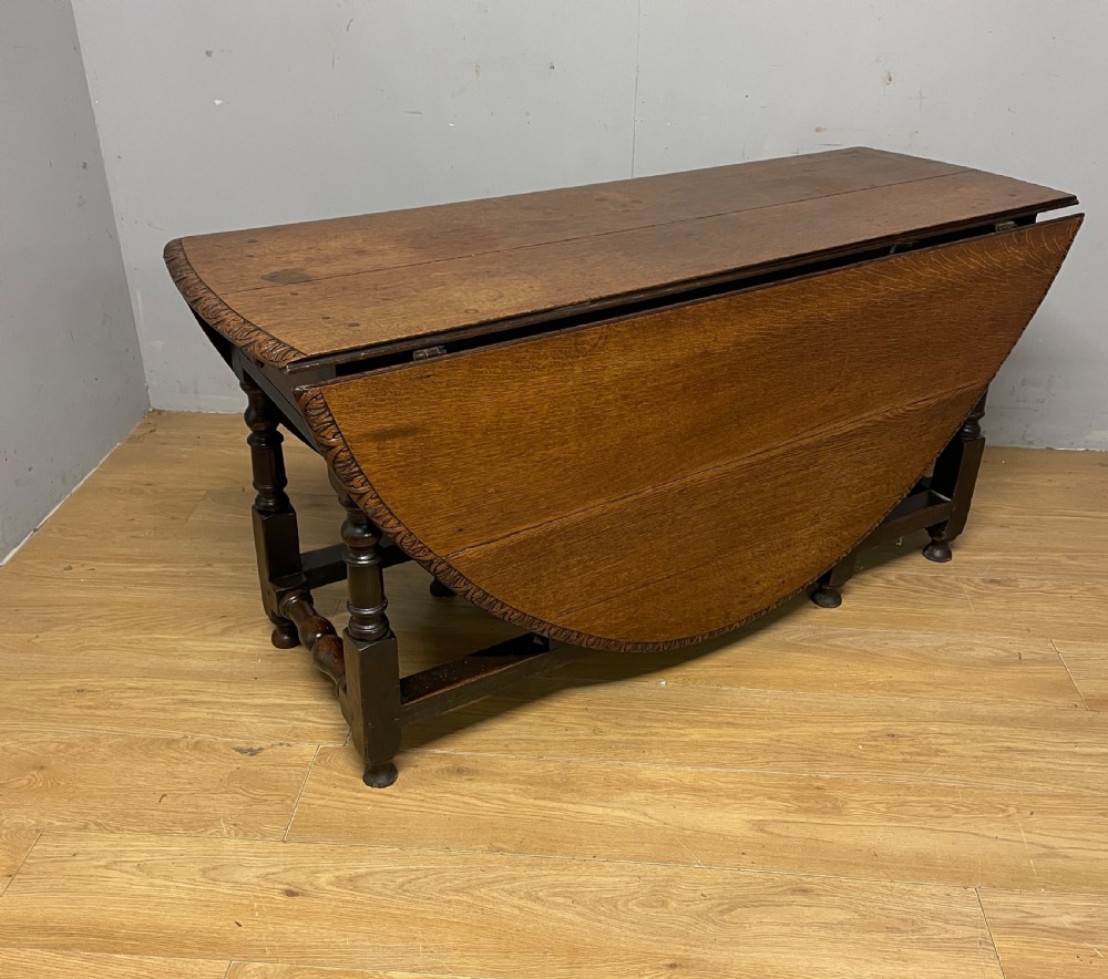 A large 19th-century dark oak drop-leaf dining table featuring turned gatelegs and a carved egg-and-dart motif along the oval table top border. View VII