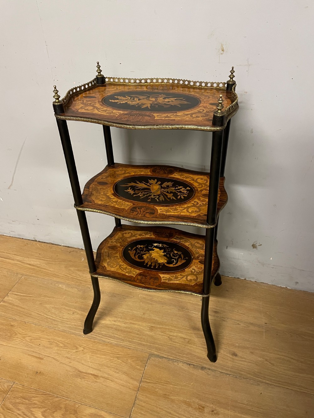 A three-tiered French etagere table featuring detailed floral marquetry wood inlays, dark turned supports, and a top shelf finished with a pierced brass gallery.