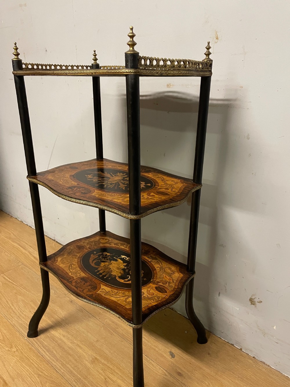A three-tiered French etagere table featuring detailed floral marquetry wood inlays, dark turned supports, and a top shelf finished with a pierced brass gallery. View IV