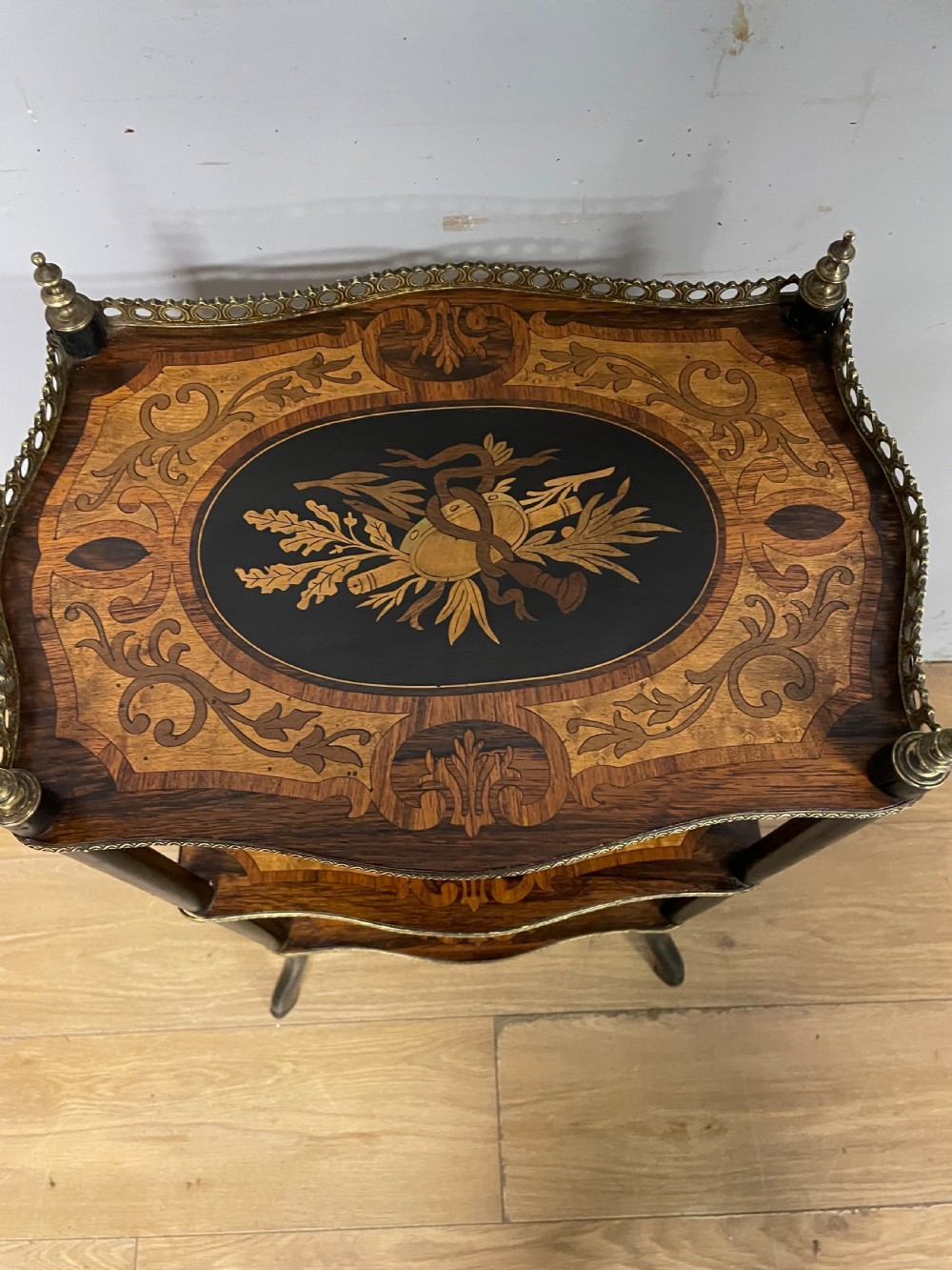 A three-tiered French etagere table featuring detailed floral marquetry wood inlays, dark turned supports, and a top shelf finished with a pierced brass gallery. View VI