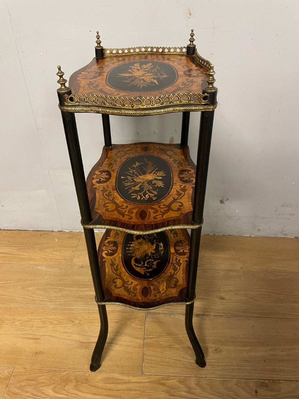 A three-tiered French etagere table featuring detailed floral marquetry wood inlays, dark turned supports, and a top shelf finished with a pierced brass gallery. View IX