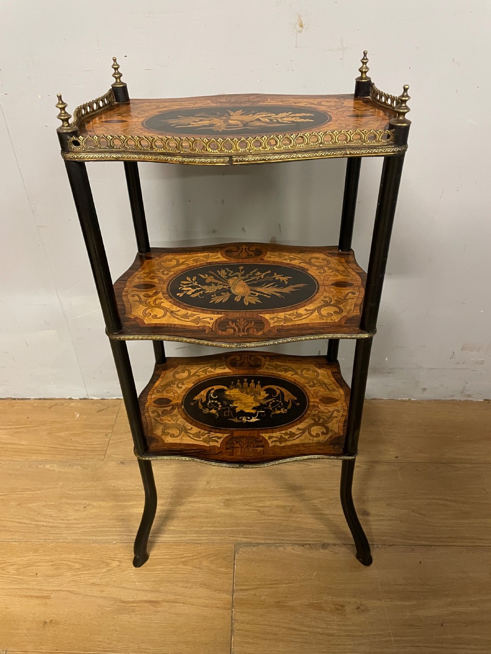 A three-tiered French etagere table featuring detailed floral marquetry wood inlays, dark turned supports, and a top shelf finished with a pierced brass gallery. View X