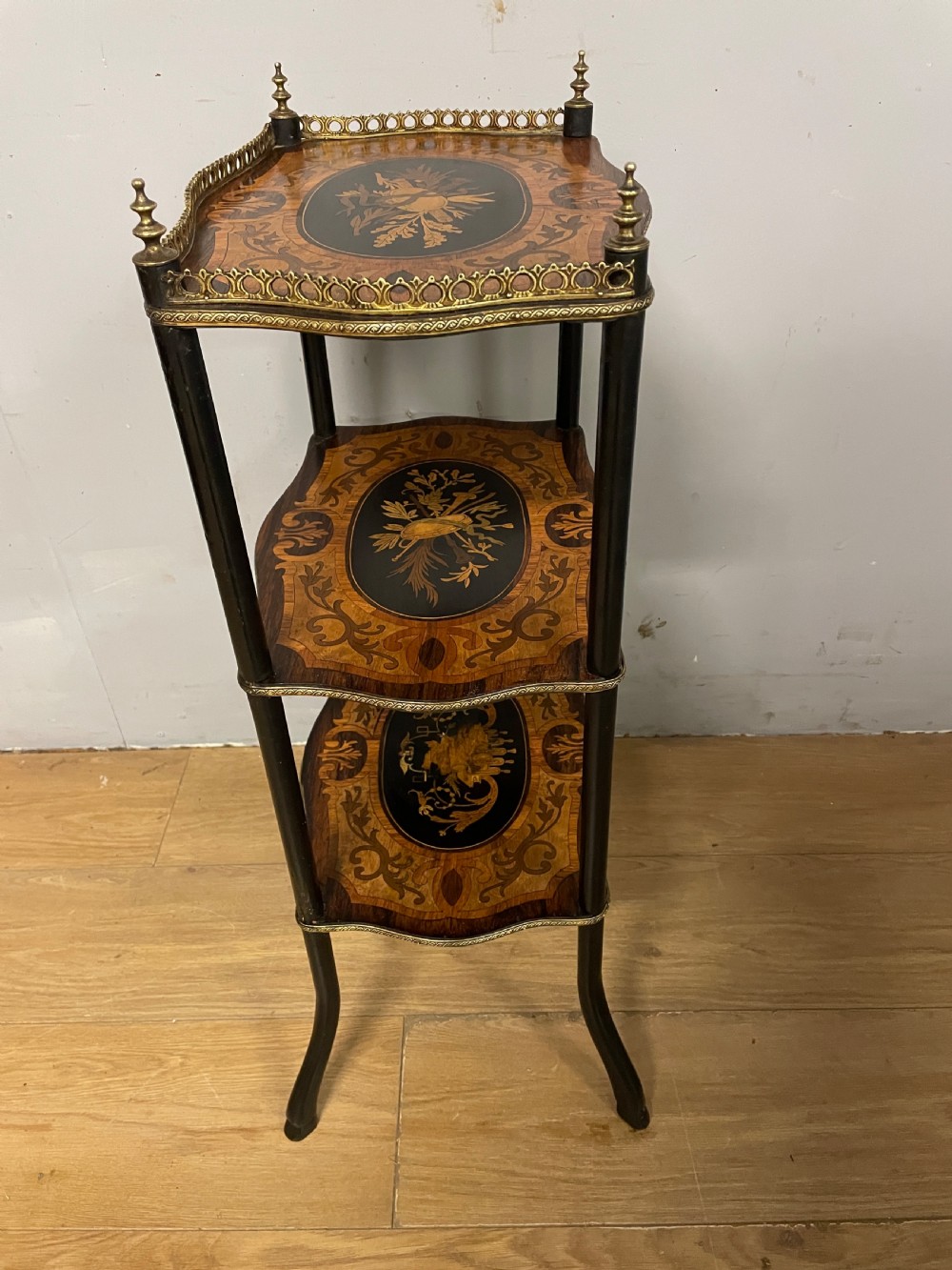 A three-tiered French etagere table featuring detailed floral marquetry wood inlays, dark turned supports, and a top shelf finished with a pierced brass gallery. View XI
