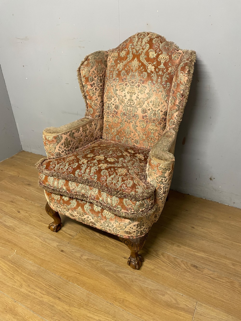 An early twentieth-century Georgian style wing armchair upholstered in patterned terracotta velvet with carved cabriole front legs ending in ball and claw feet.