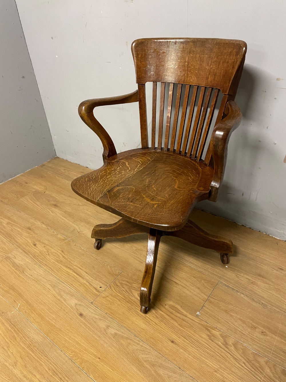 An Edwardian solid oak revolving and tilting office chair with a curved backrest, vertical spindles, and castors.