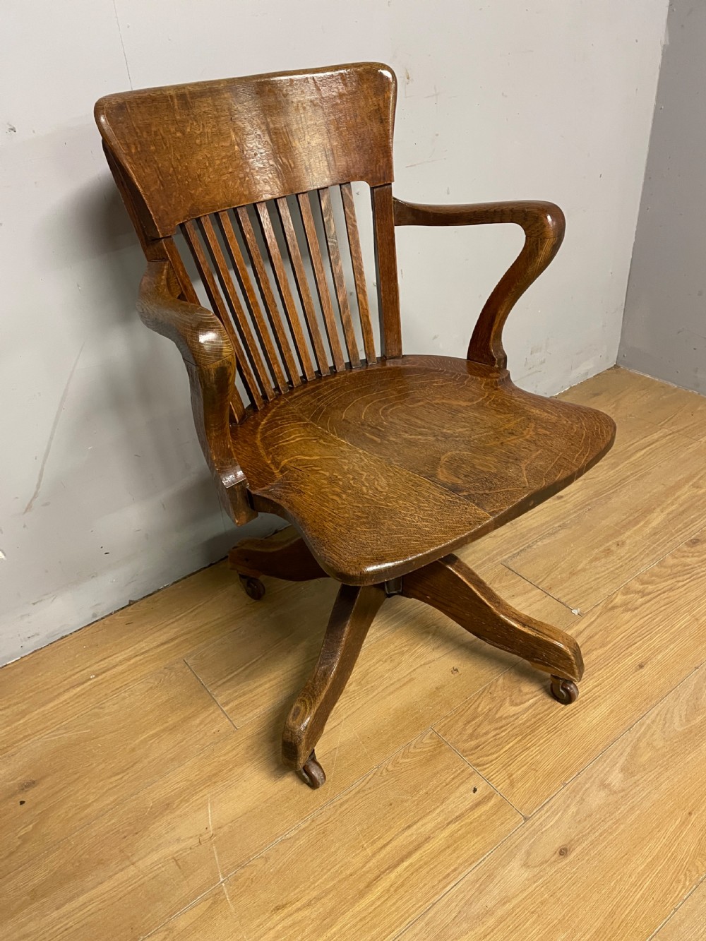 An Edwardian solid oak revolving and tilting office chair with a curved backrest, vertical spindles, and castors. View II