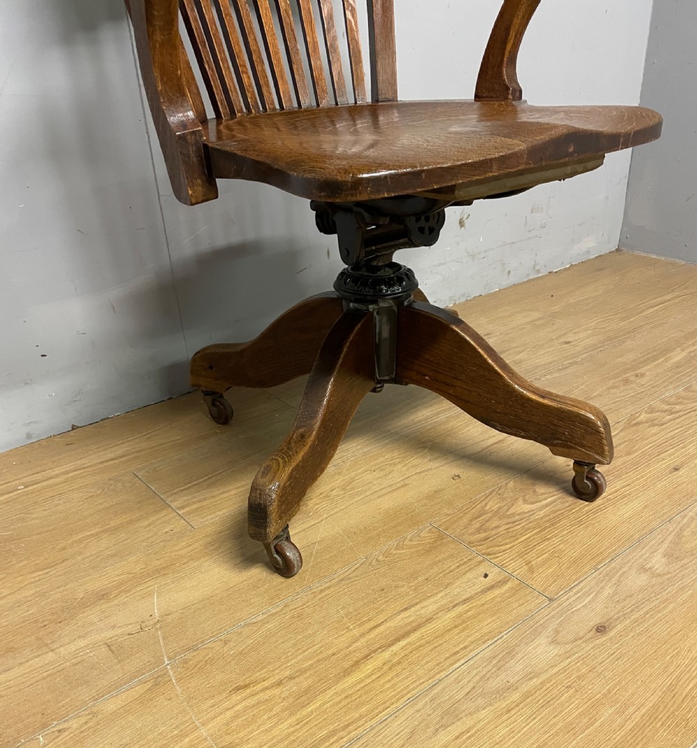 An Edwardian solid oak revolving and tilting office chair with a curved backrest, vertical spindles, and castors. View III