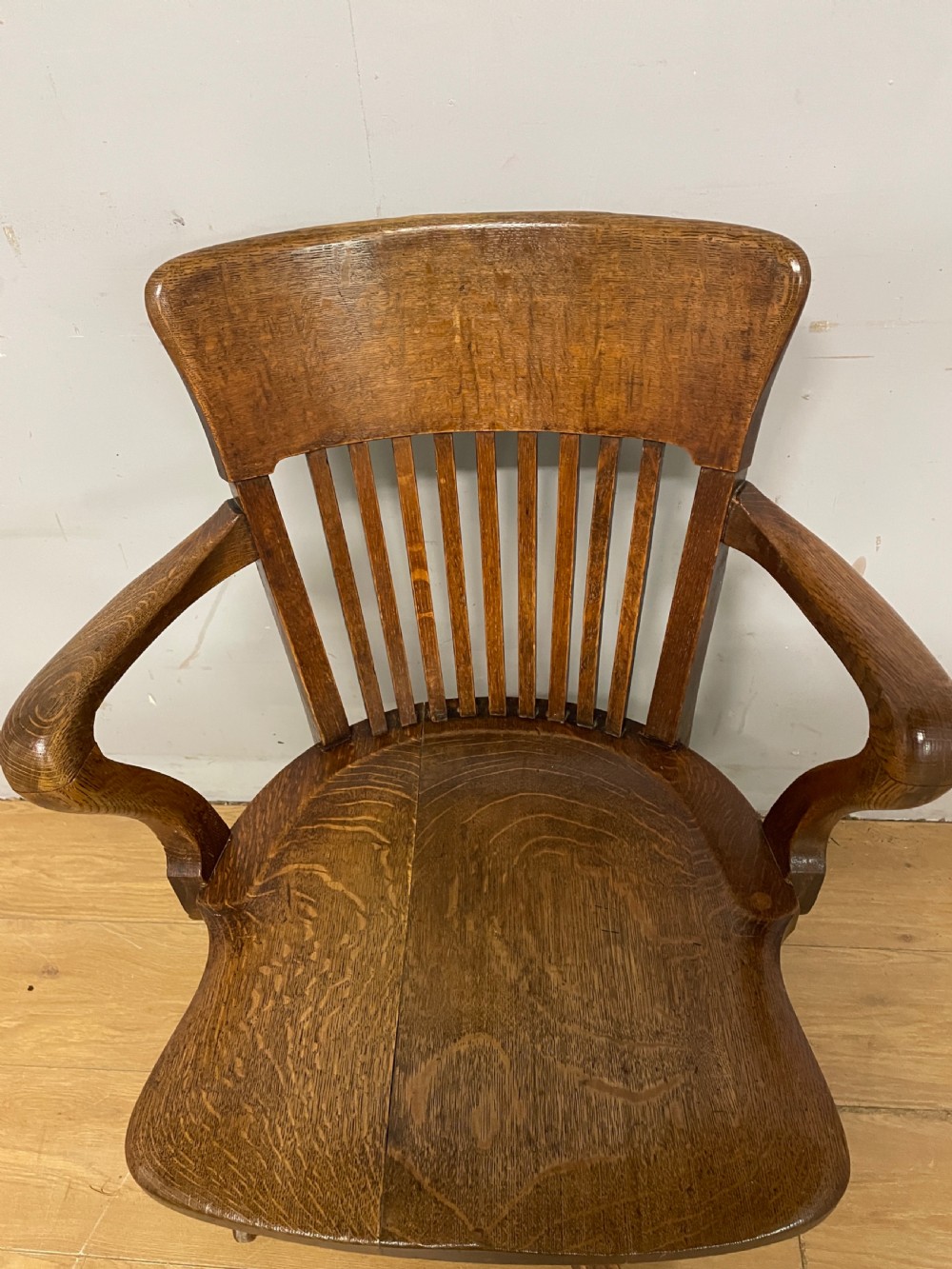 An Edwardian solid oak revolving and tilting office chair with a curved backrest, vertical spindles, and castors. View IV