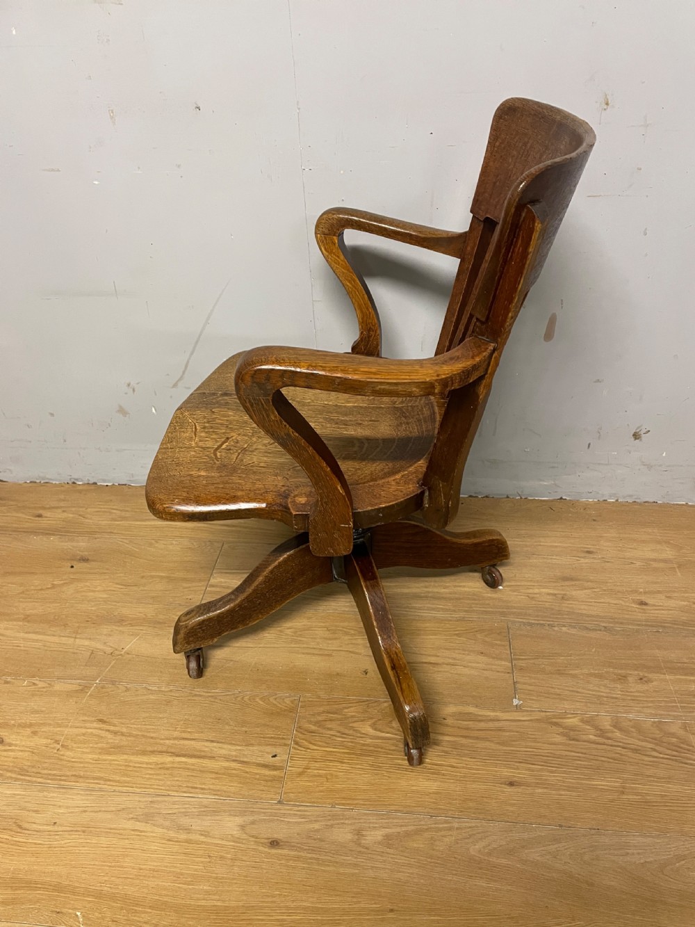 An Edwardian solid oak revolving and tilting office chair with a curved backrest, vertical spindles, and castors. View V