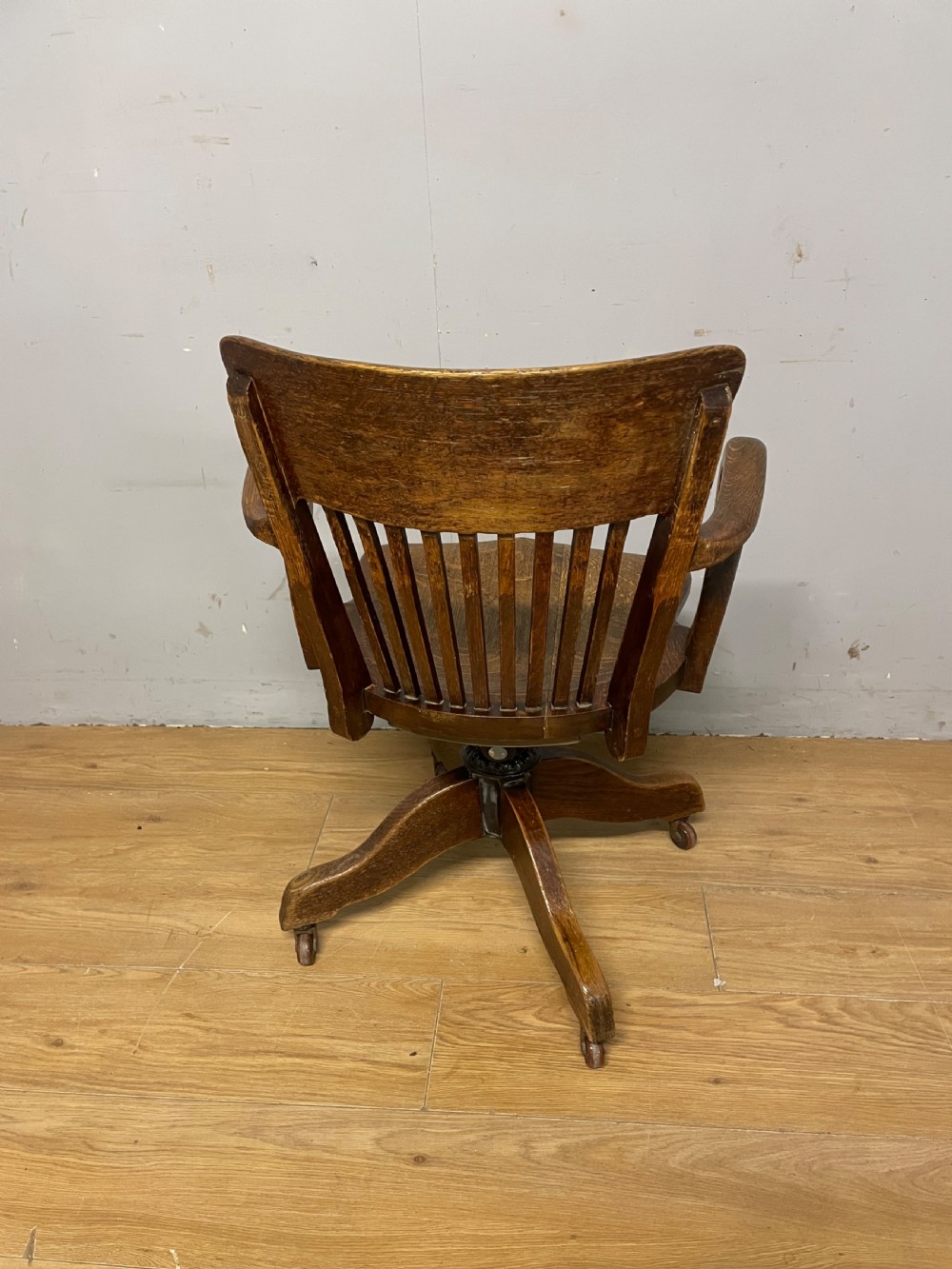 An Edwardian solid oak revolving and tilting office chair with a curved backrest, vertical spindles, and castors. View VI